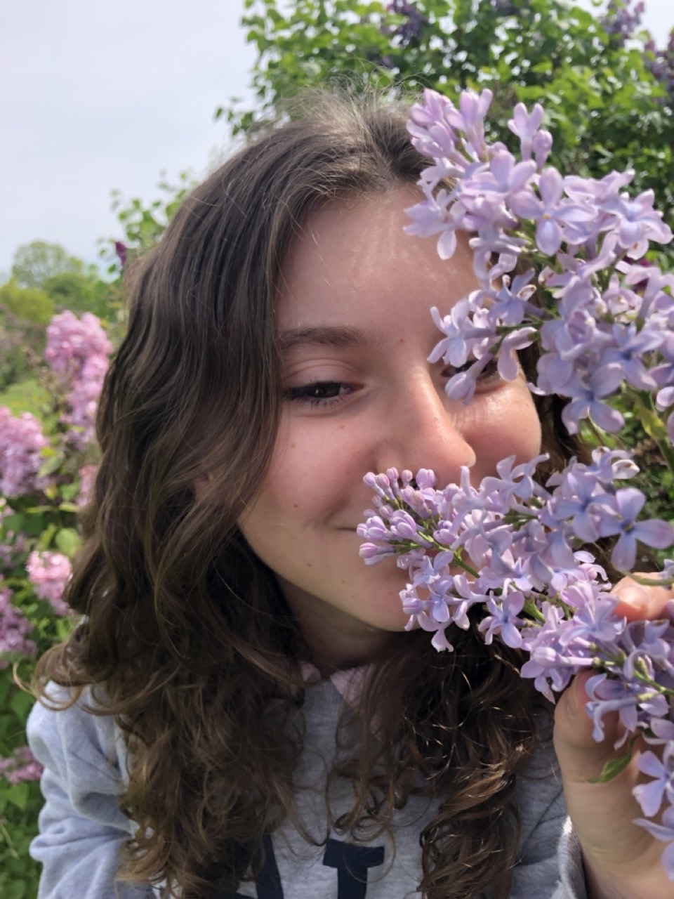 Girl crouches behind flowers to smell them